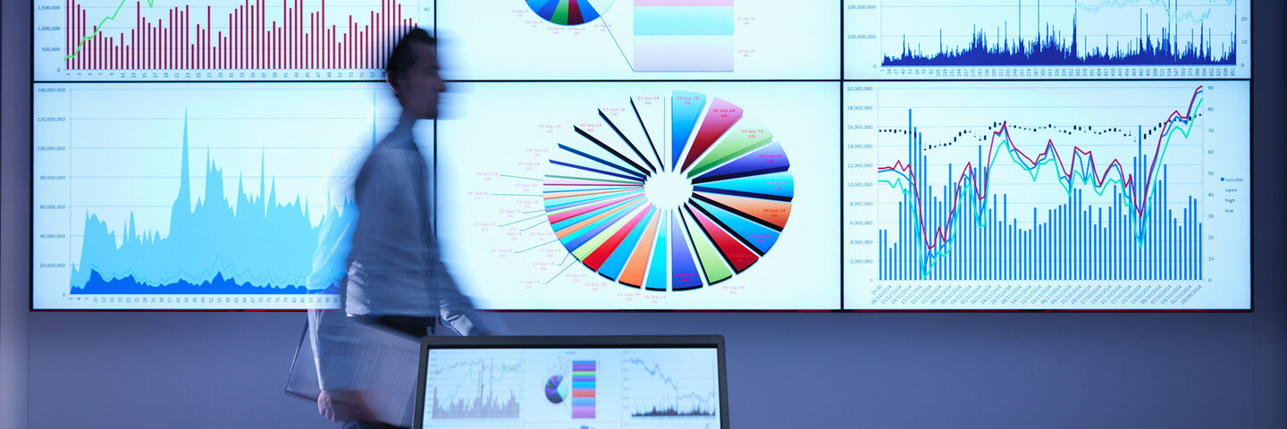 A man in front of a large screen with data and charts on it.