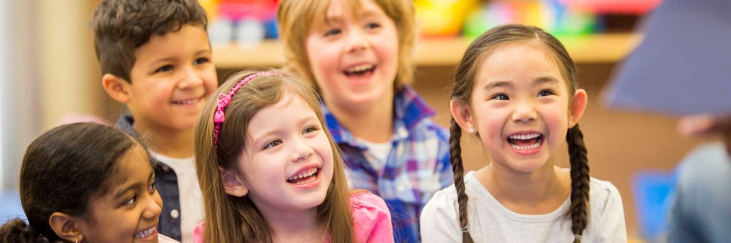 A multi-ethnic group of elementary age children listening to their teacher read a storybook in class.