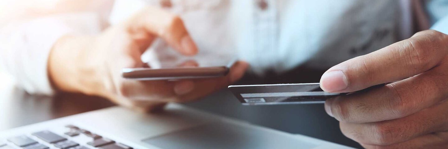Student dialing on a smart phone while holding a credit card.