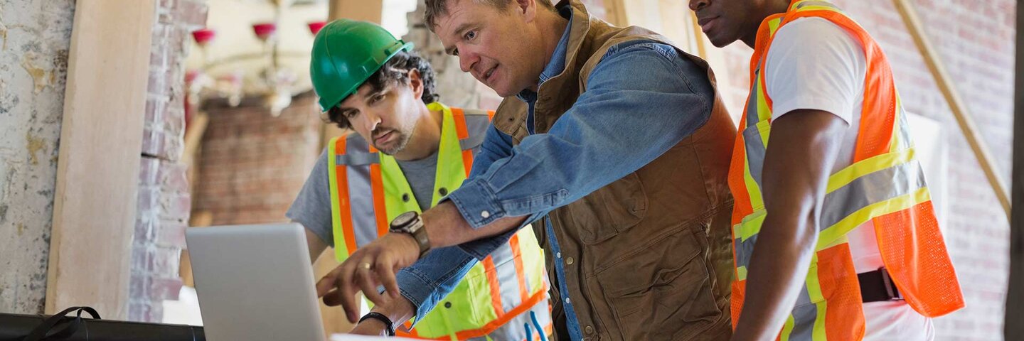 Foreman discussing plan on laptop with tradesmen at construction site