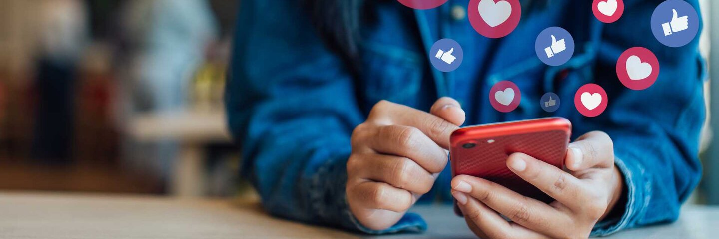 hands holding a smart phone with "like" and "love" emojis floating up from it