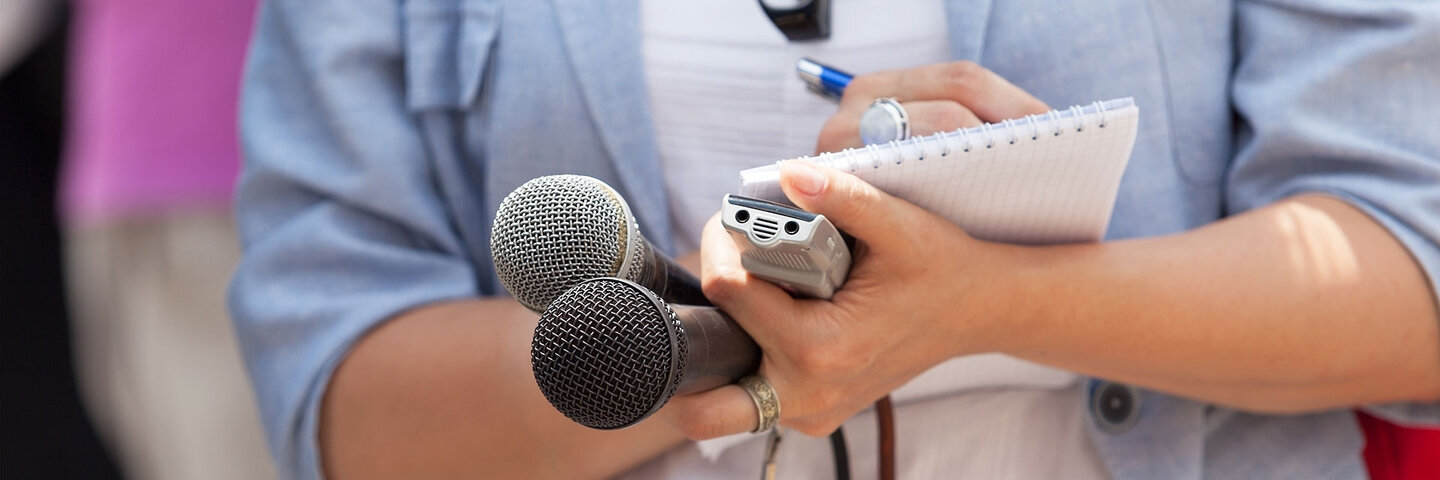 Woman holding microphones and recorder, writing on note pad