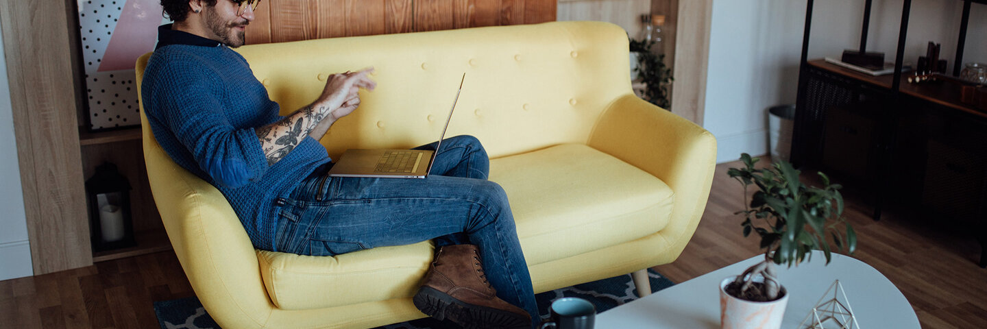 hip guy on a yellow couch engrossed in a zoom meeting