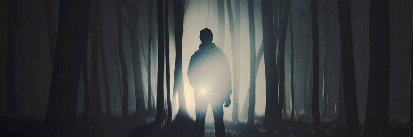 Man walking in the foggy woods at night with a flashlight